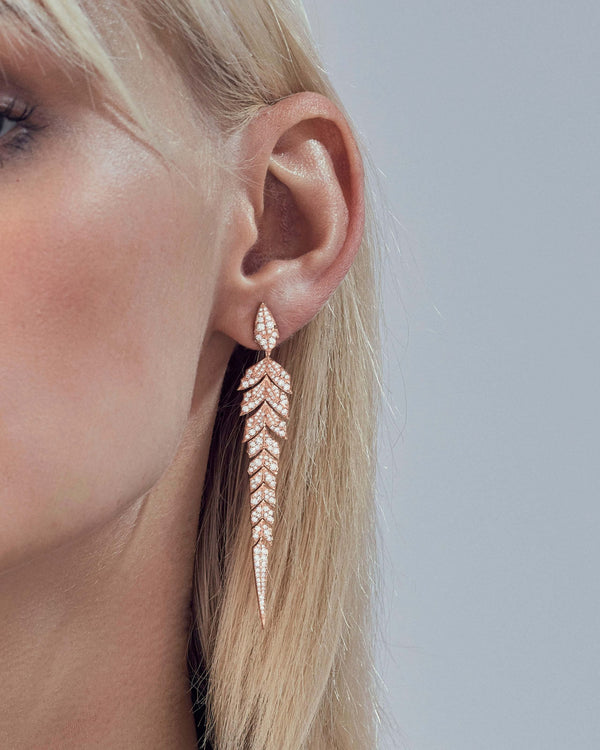 Close-up of white diamond pavé and articulated tail feather motif on rose gold feather jewellery long drop earrings