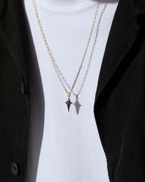 Model wearing Stephen Webster New Cross gold pendant with black diamonds — pendant centered on chest, highlighting size and sparkle