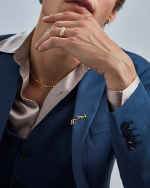 Model wearing Stephen Webster Smoking Gun gold tie clip on suit — clip visible on blazer, showing style and scale