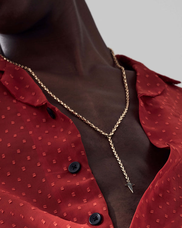 Close-up of model’s neck wearing Stephen Webster New Cross pendant — showing black diamond detail, gold finish and chain texture