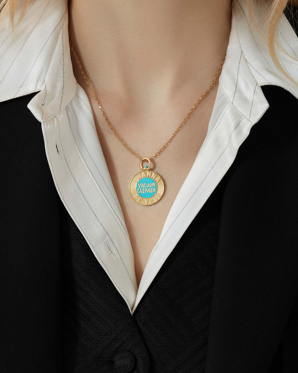 Close-up of Stephen Webster Vacuum Cleaner 18 ct gold pendant worn on model’s neck, highlighting turquoise and purple enamel vinyl design and engraved lettering