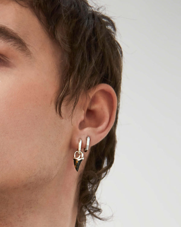 Styled image of Stephen Webster Unithorn Tiger Iron Charm paired with a sterling silver earring — men’s jewellery styling